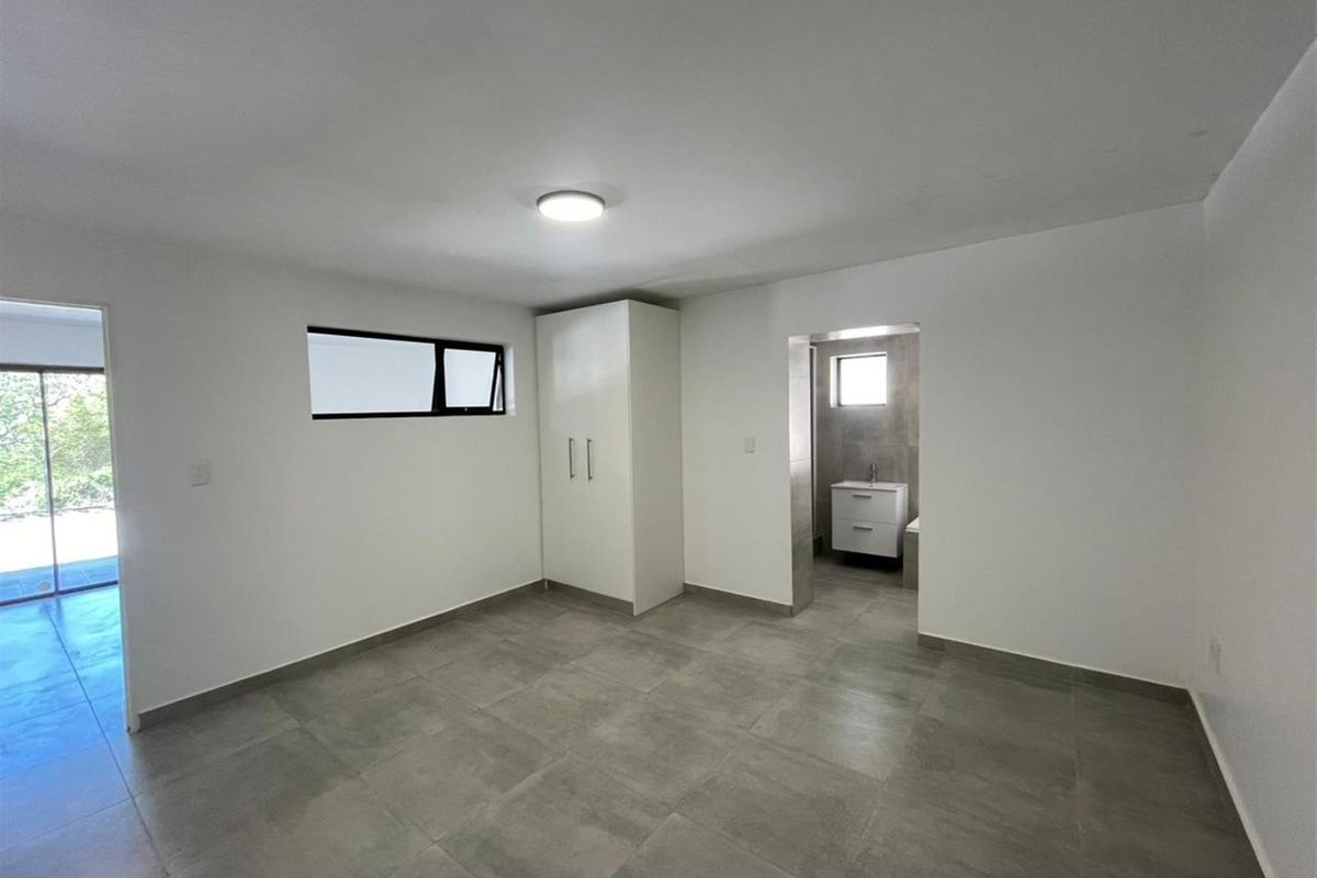 A clean, modern bedroom featuring neutral tiled flooring, a built-in wardrobe, and direct access to an en-suite bathroom.