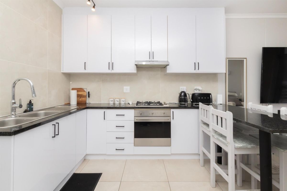 Modern kitchen featuring white cabinetry, dark stone countertops, stainless steel appliances, gas hob, and neutral tiled finishes.