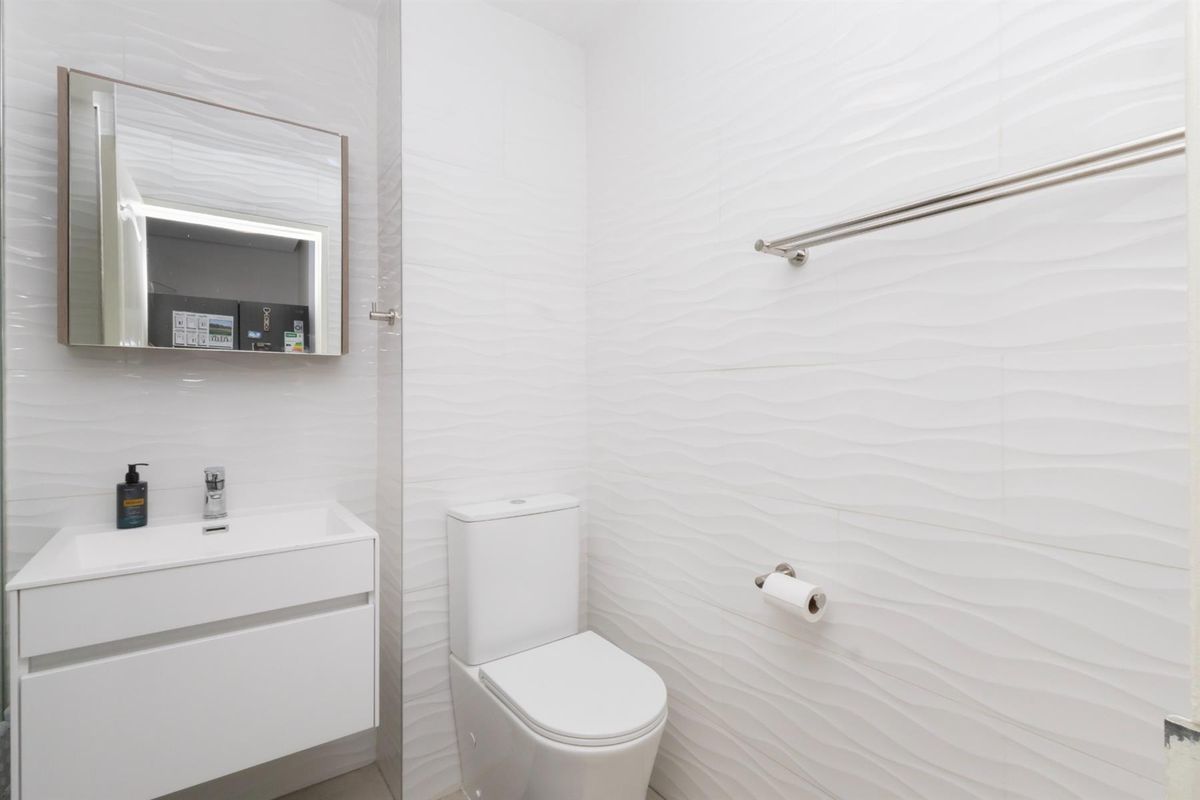 Modern bathroom featuring a wall-mounted vanity, basin, back-to-wall toilet, and contemporary textured white wall tiles.