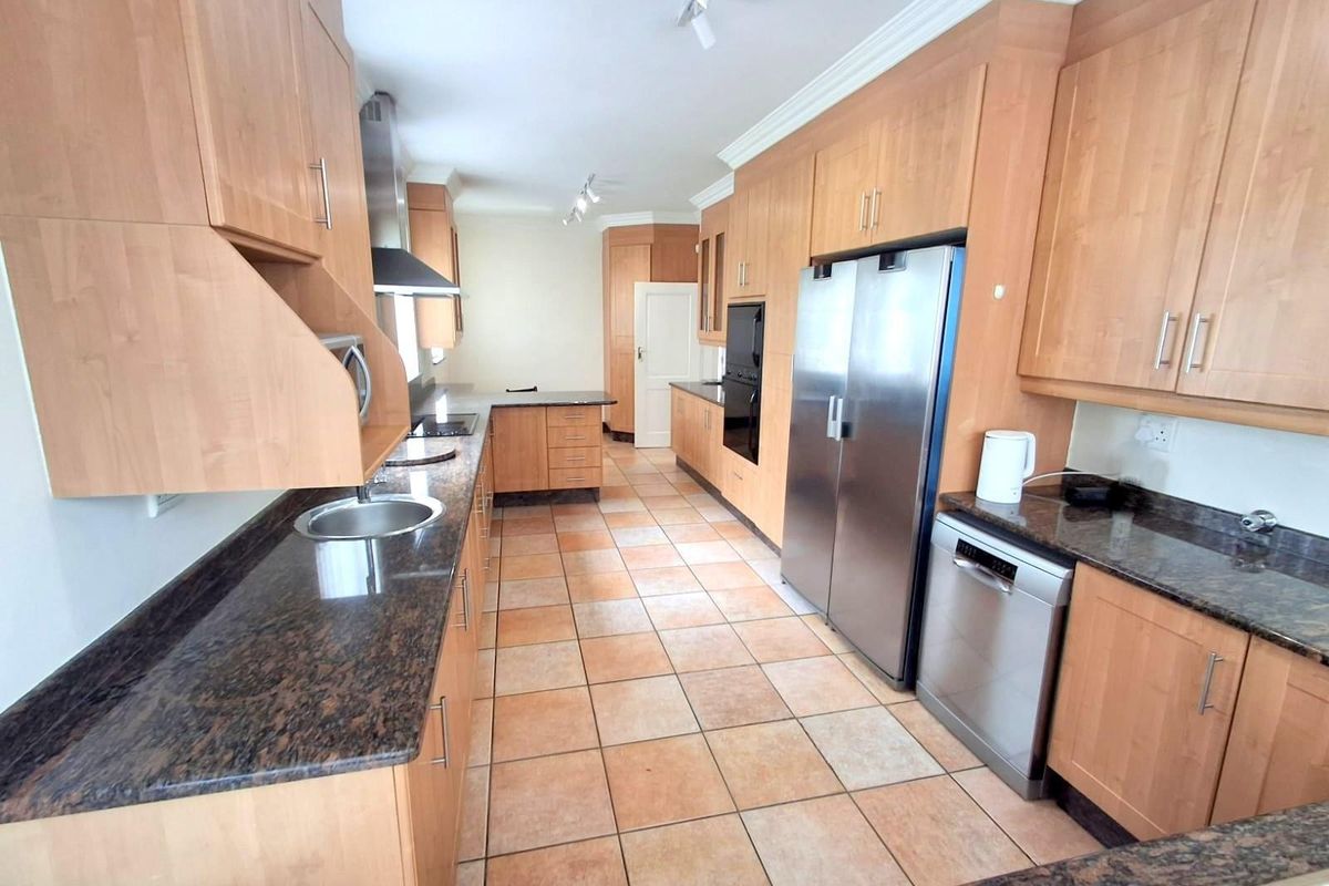 A spacious kitchen featuring light wood cabinetry, dark granite countertops, tiled flooring, and integrated stainless steel appliances.