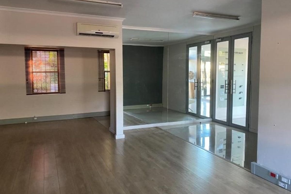 Spacious commercial office area featuring laminate flooring, mirrored wall, split-system air conditioning, and glass-panelled double doors providing natural light and access.