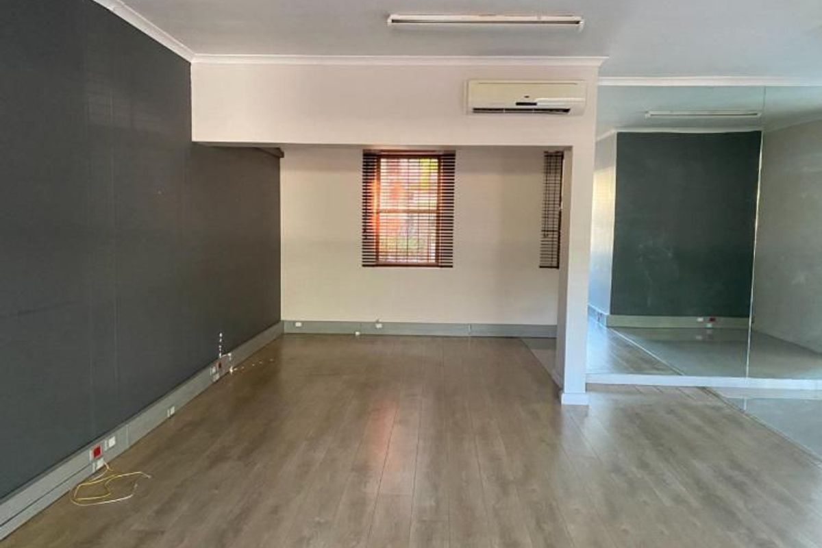 An open-plan commercial space featuring laminate flooring, a mirrored wall, and a split-system air conditioner, suitable for various business or studio uses.