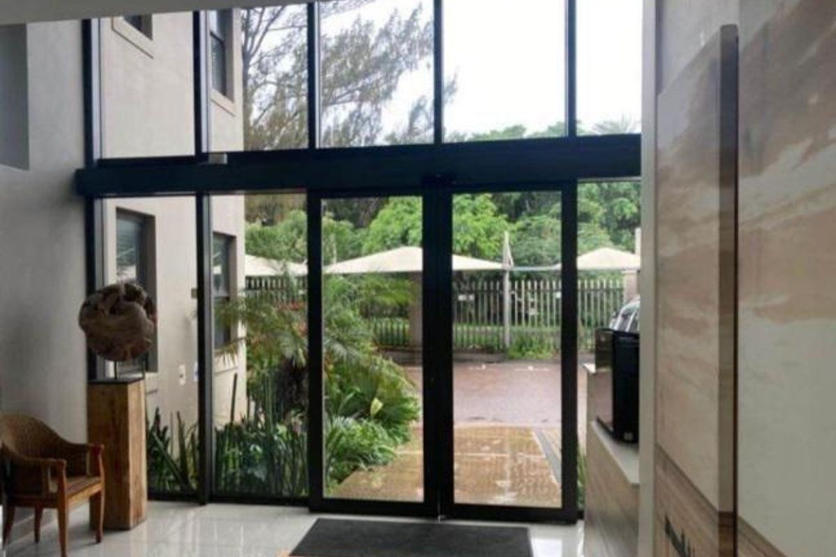 Bright commercial entrance featuring double-volume floor-to-ceiling glass windows and automatic sliding doors, providing a welcoming and modern reception area.