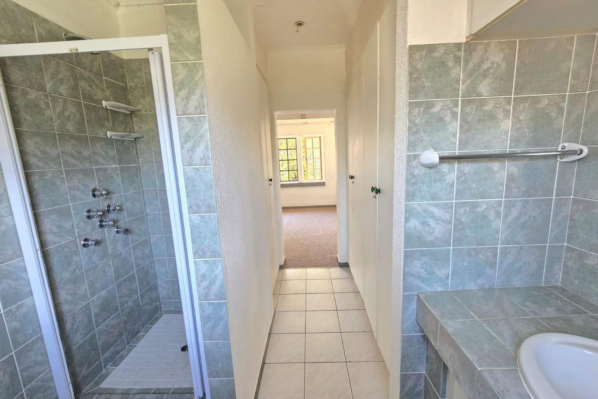 A functional bathroom featuring a tiled shower enclosure, built-in vanity, and tiled flooring, leading into an adjacent room.