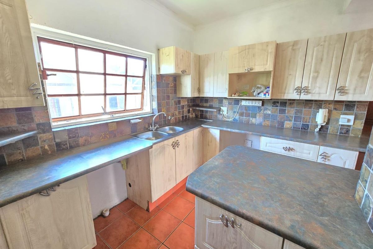 A functional kitchen featuring light wood-finish cabinetry, stone-look laminate countertops, a double basin sink, and a tiled backsplash with terracotta floor tiles.