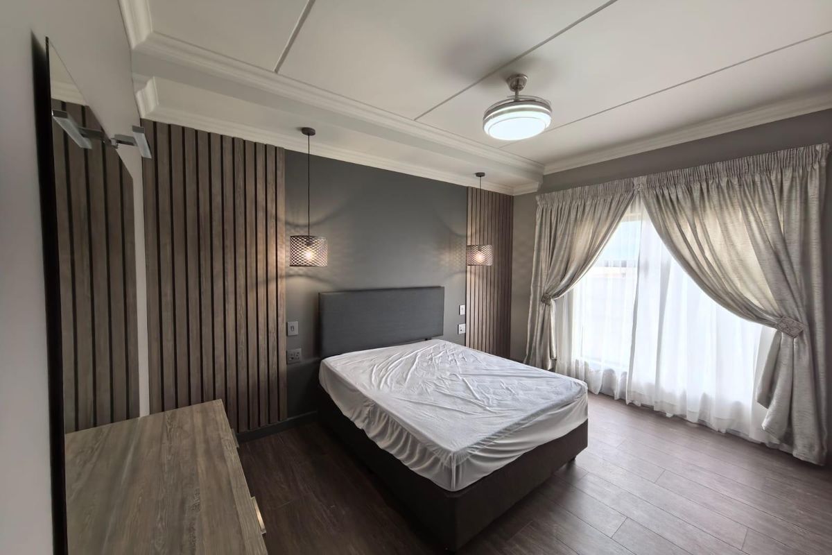 Modern bedroom featuring wood-slat accent wall paneling, recessed ceiling detail, integrated pendant lighting, and wood-look flooring.