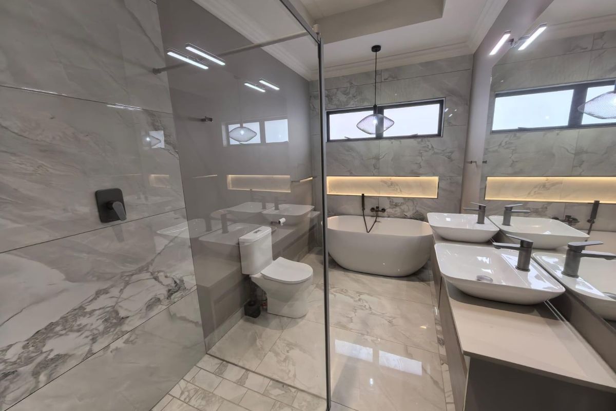 Modern luxury bathroom featuring a freestanding bathtub, glass-enclosed walk-in shower, double vanity with vessel sinks, and elegant marble-style tiling throughout.