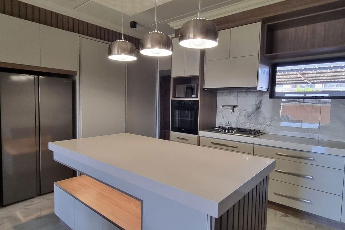 Modern kitchen featuring a central island, stone countertops, built-in oven, gas hob, and sleek cabinetry with integrated lighting.