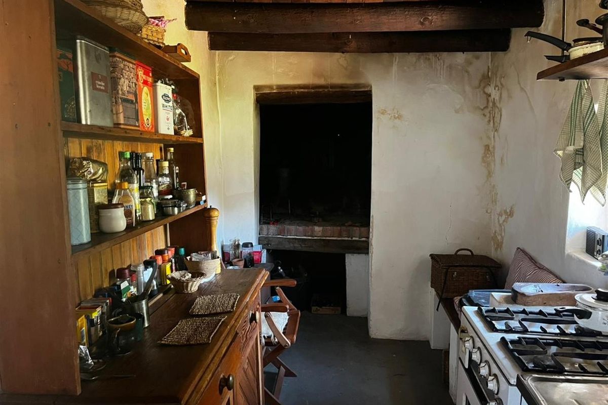 Rustic kitchen area featuring exposed timber ceiling beams, a built-in hearth, and a gas stove, showing signs of significant wear and wall damage.
