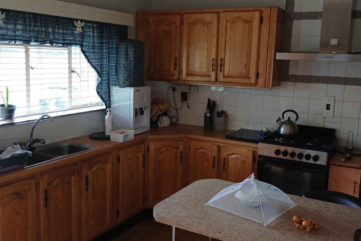A functional kitchen featuring traditional timber cabinetry, tiled splashbacks, a stainless steel sink, and a built-in gas stove with an extractor fan.