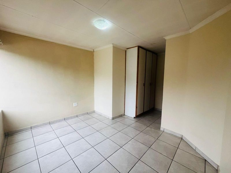 A clean, empty bedroom featuring neutral tiled flooring and a built-in wardrobe, offering a versatile space ready for personalization.