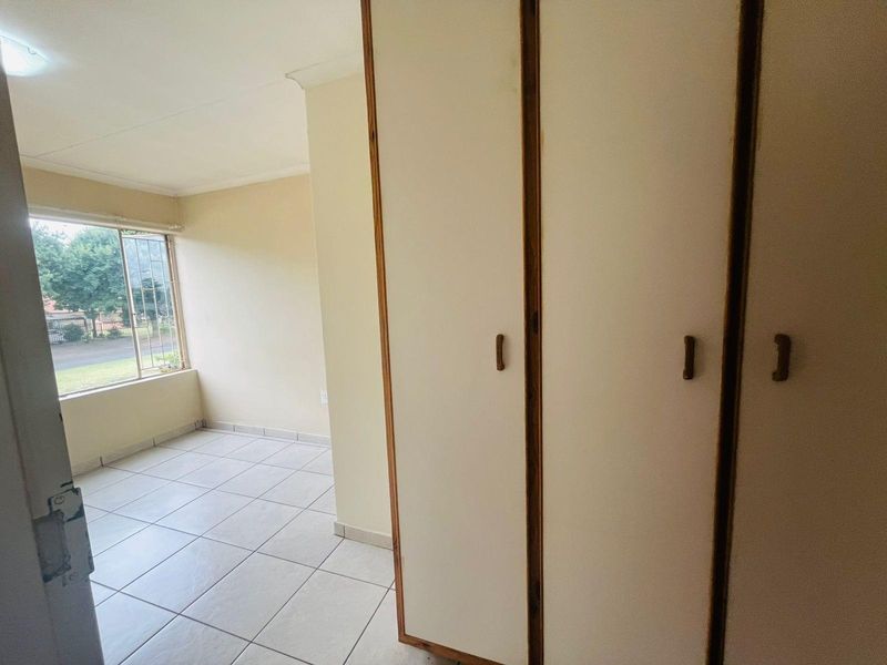 A bedroom featuring tiled flooring and built-in cupboards with wooden trim, offering natural light through a large window.