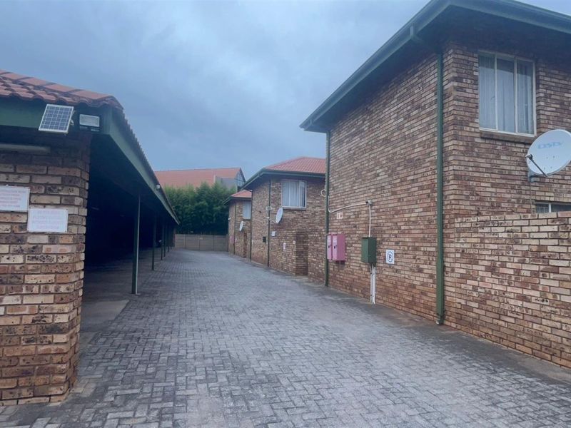 A view of the townhouse complex driveway featuring covered parking bays and face-brick exterior walls.