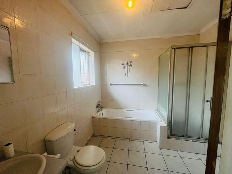 A functional bathroom featuring a built-in bathtub, separate shower enclosure, toilet, and vanity basin with full-height wall tiling.