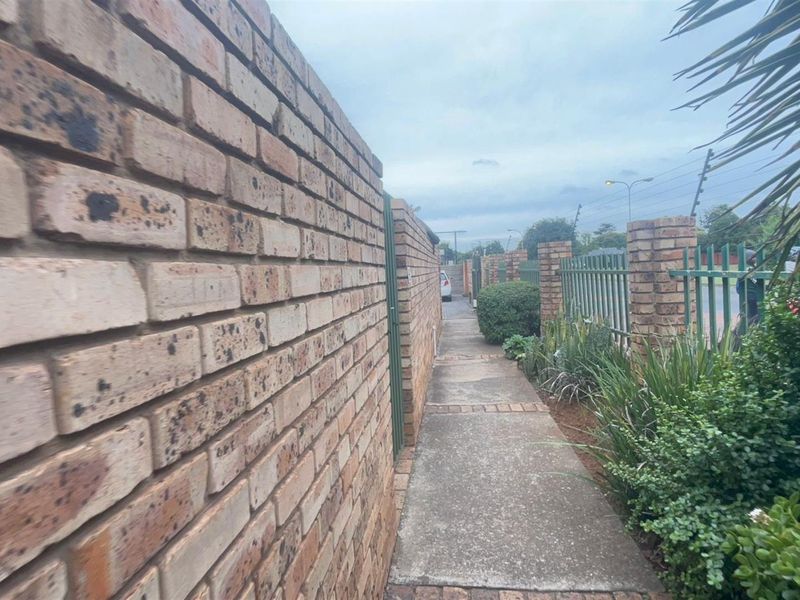 A narrow exterior walkway featuring a face-brick boundary wall and metal security fencing along the property perimeter.