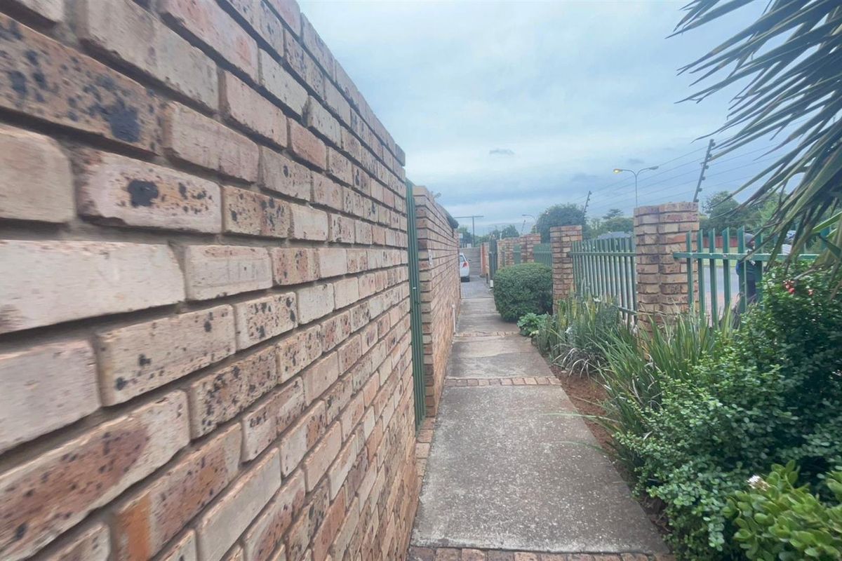 A narrow exterior walkway featuring a face-brick boundary wall and metal security fencing along the property perimeter.