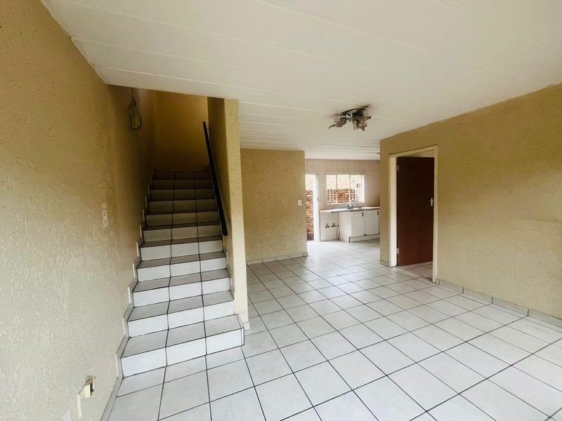 Open plan living area featuring tiled flooring, a staircase with tiled steps, and a view through to the kitchen area.