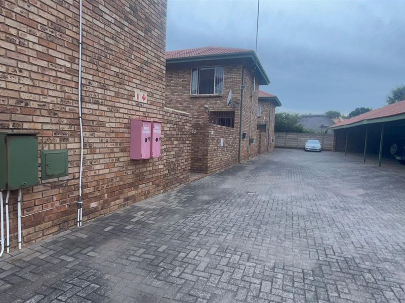 Exterior view of the townhouse complex driveway featuring paved parking areas, covered carports, and face-brick building facades.