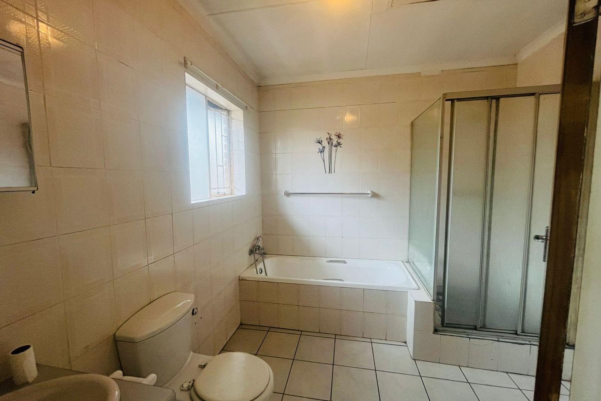 A functional bathroom featuring a built-in bathtub, separate shower enclosure, toilet, and vanity basin with full-height wall tiling.