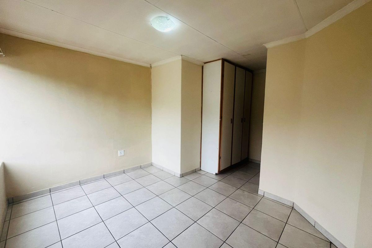 A clean, empty bedroom featuring neutral tiled flooring and a built-in wardrobe, offering a versatile space ready for personalization.
