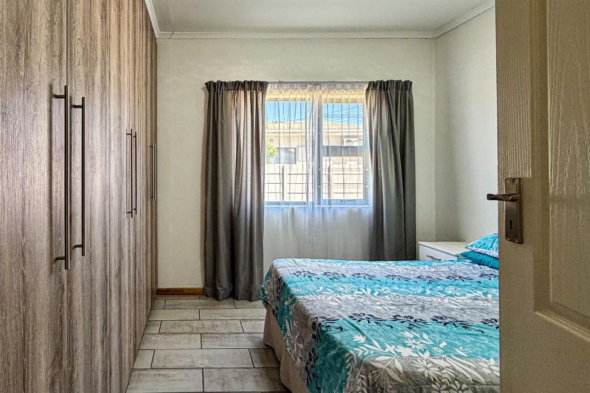 A well-maintained bedroom featuring floor-to-ceiling built-in wooden wardrobes and tiled flooring, providing ample storage and a clean, functional living space.