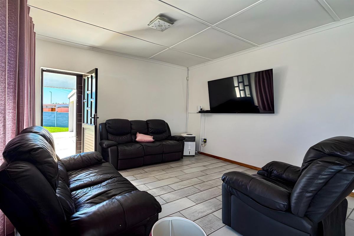 A living room featuring tiled flooring, a ceiling-mounted light fixture, and direct access to an outdoor area through a glass-paneled door.