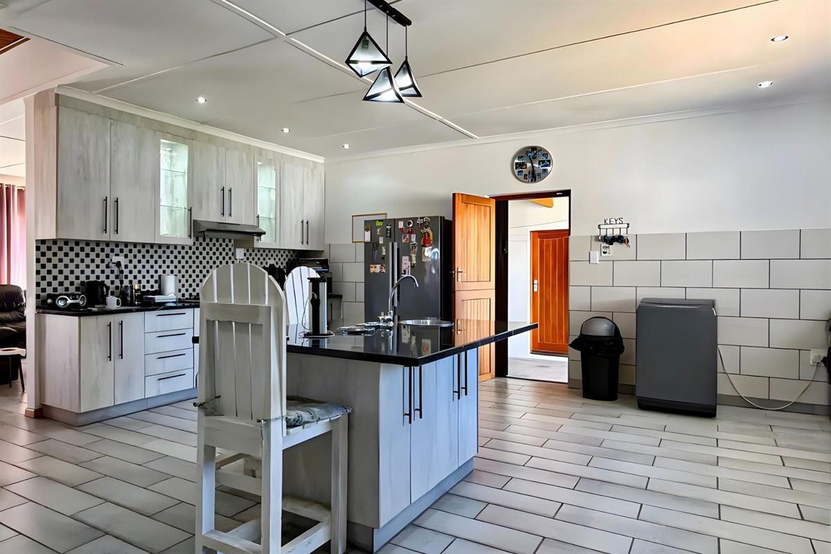 A functional kitchen featuring a central island with a dark countertop, light-toned cabinetry, tiled backsplash, and modern pendant lighting.