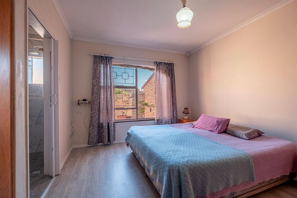 A bedroom featuring light-toned laminate flooring, a window with security bars, and an adjoining en-suite bathroom.