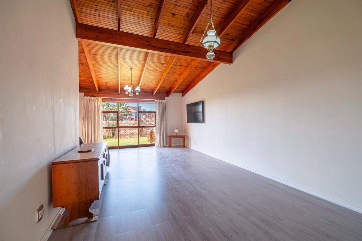 Spacious living room featuring high vaulted timber beam ceilings, modern laminate flooring, and large sliding glass doors providing access to the rear garden.