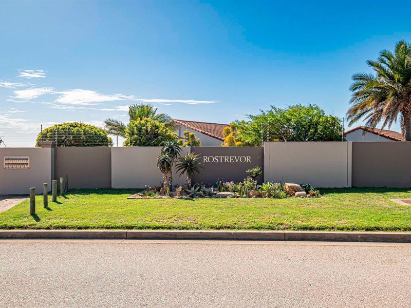 Street view of the Rostrevor complex entrance, featuring a well-maintained perimeter wall, electric fencing, and landscaped garden area.