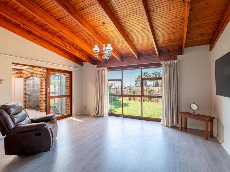 Spacious living room featuring exposed timber beam ceilings, light wood-look flooring, and large windows providing natural light and views of the rear garden.