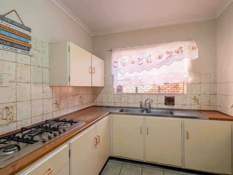 A dated kitchen featuring a built-in gas hob, double stainless steel sink, and original cabinetry with tiled splashbacks.