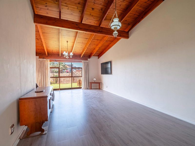 Spacious living room featuring high vaulted timber beam ceilings, modern laminate flooring, and large sliding glass doors providing access to the rear garden.