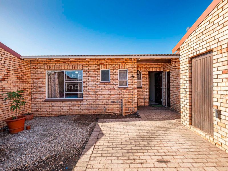 A view of the exterior rear courtyard featuring face-brick walls, paved patio area, and access to the main dwelling.