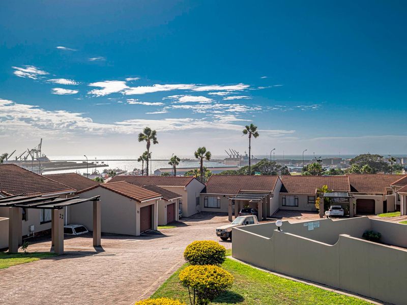 Elevated view of a townhouse complex featuring paved driveways, tiled roofs, and a distant harbor and ocean outlook.