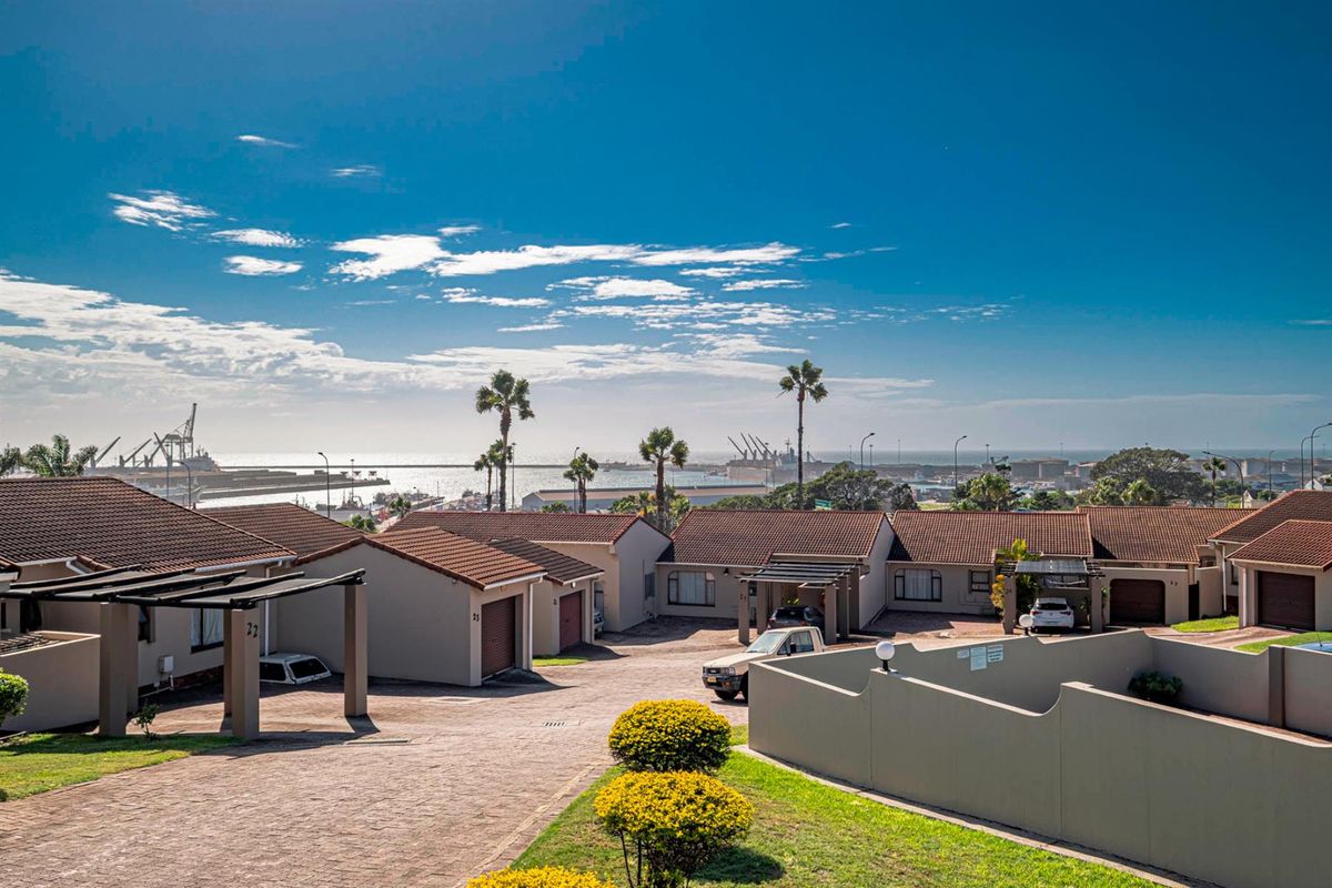 Elevated view of a townhouse complex featuring paved driveways, tiled roofs, and a distant harbor and ocean outlook.