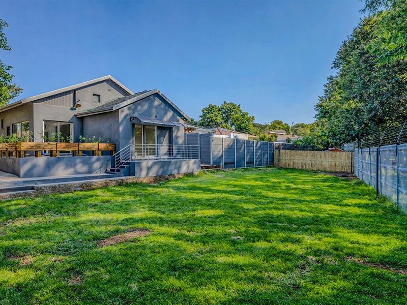 Spacious rear garden featuring a raised patio area with metal railings, well-maintained lawn, and secure perimeter fencing.
