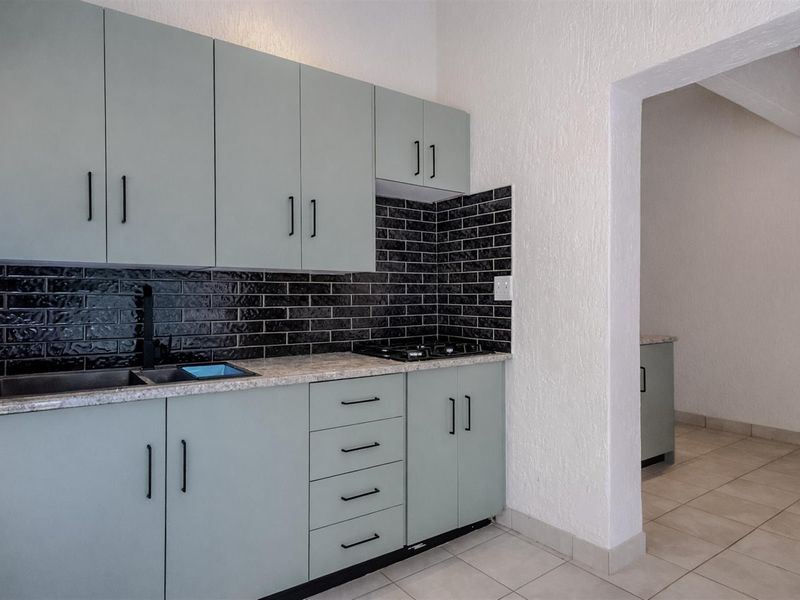 Modern kitchen featuring light green cabinetry, stone-look countertops, black subway tile backsplash, and a built-in hob, with an adjacent utility area.