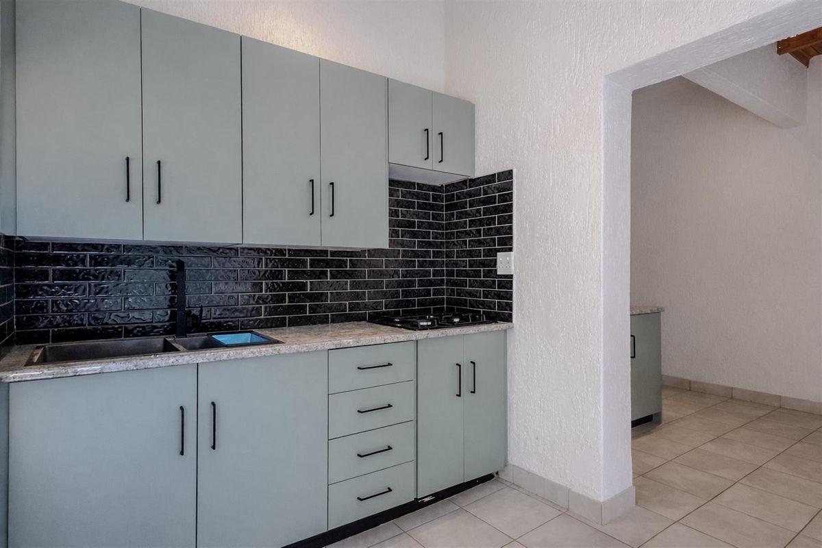 Modern kitchen featuring light green cabinetry, stone-look countertops, black subway tile backsplash, and a built-in hob, with an adjacent utility area.