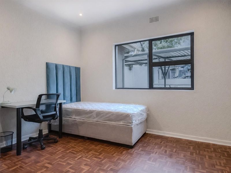 A bedroom featuring parquet flooring, a large window with dark frames, and a built-in ceiling vent.