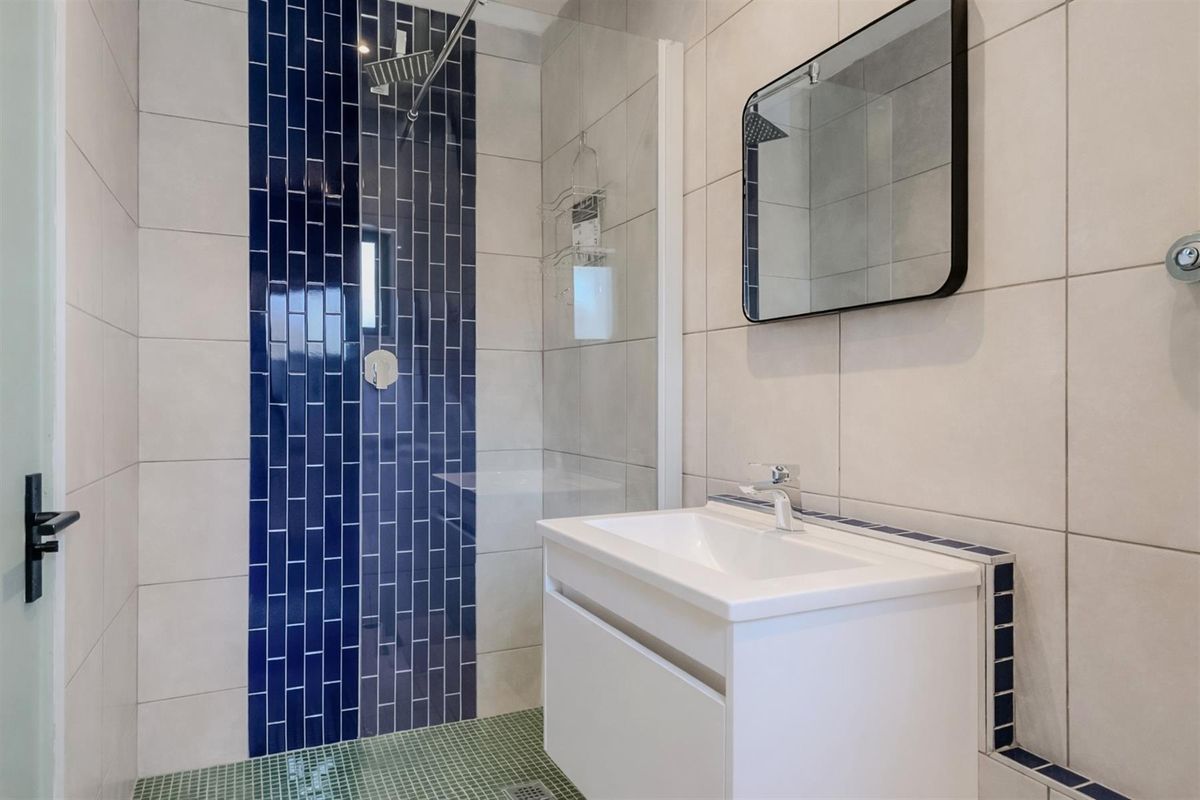 Modern bathroom featuring a walk-in shower with blue accent tiling, a glass screen, and a contemporary vanity unit with a basin.