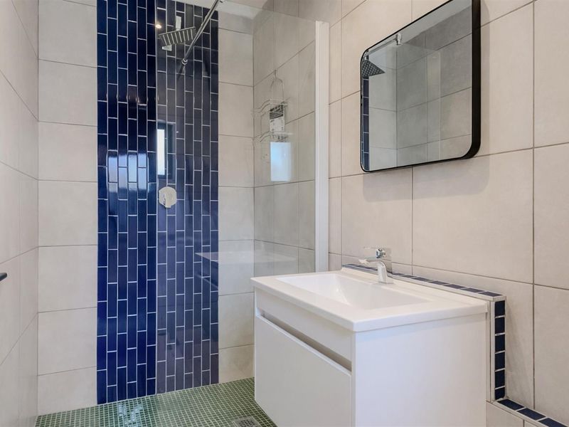 Modern bathroom featuring a walk-in shower with blue accent tiling, a glass screen, and a contemporary vanity unit with a basin.