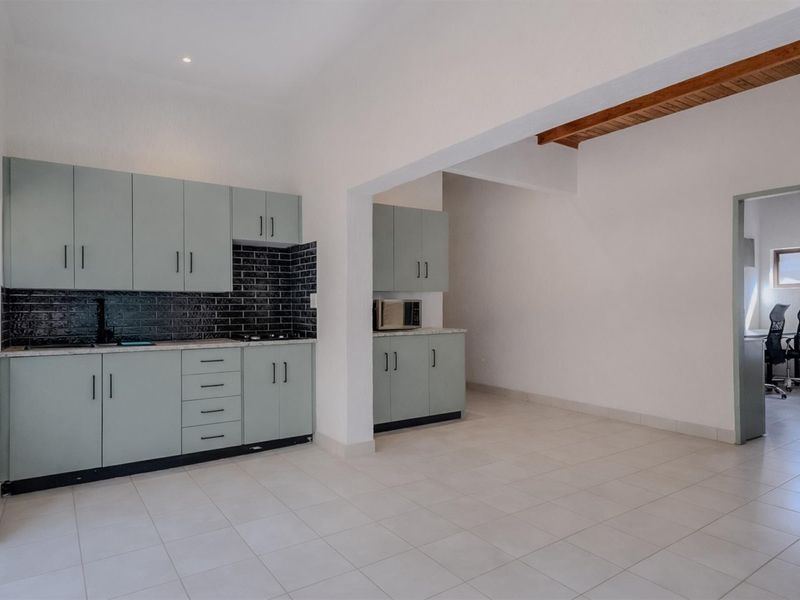 A modern kitchen featuring light green cabinetry, dark subway tile backsplash, and tiled flooring, seamlessly connected to an adjacent living or dining area.