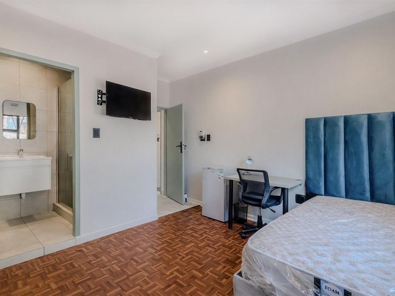 A well-maintained bedroom featuring parquet flooring, an en-suite bathroom with a shower, and a wall-mounted television.