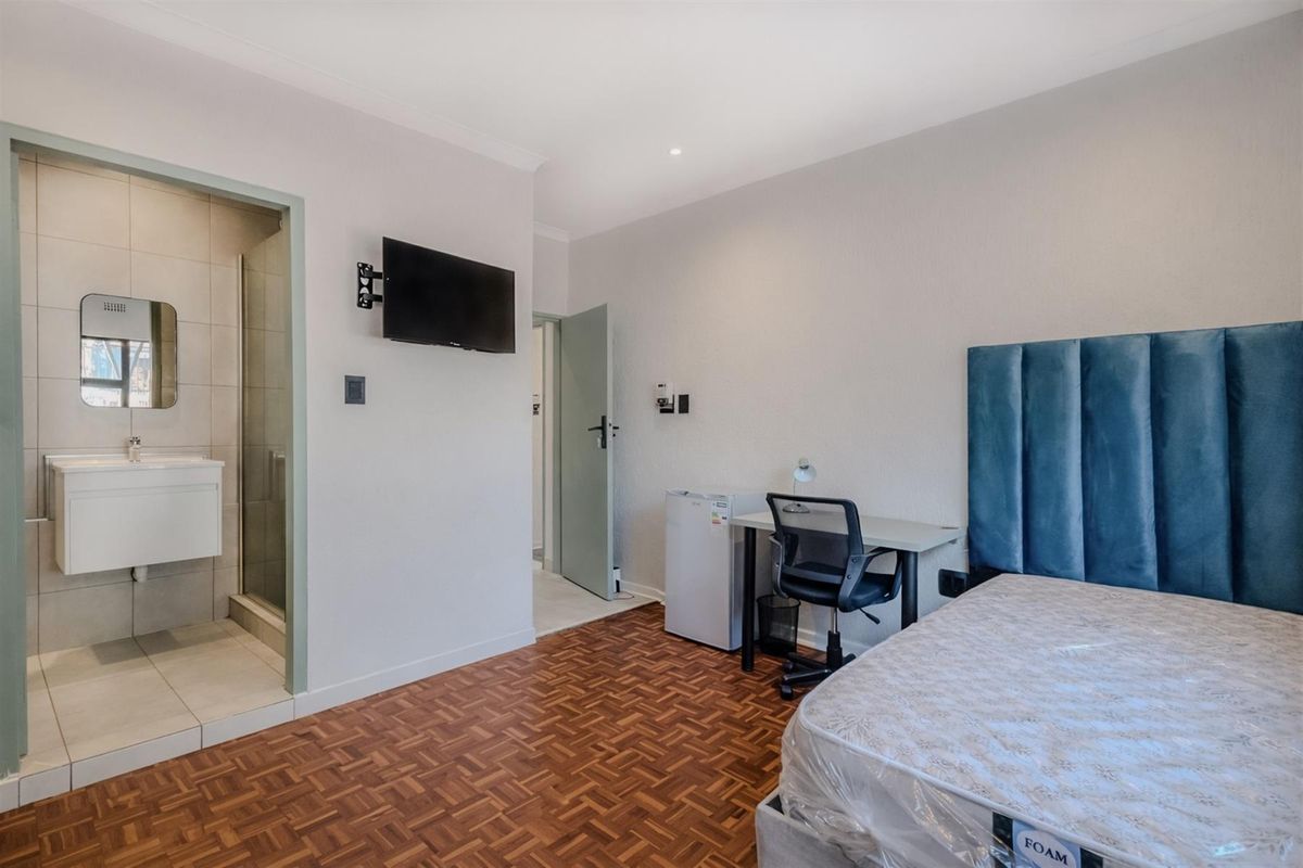 A well-maintained bedroom featuring parquet flooring, an en-suite bathroom with a shower, and a wall-mounted television.