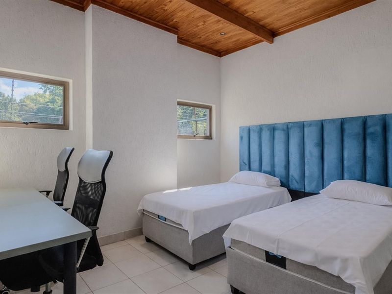 A bedroom featuring tiled flooring, a timber-paneled ceiling, and two windows providing natural light.