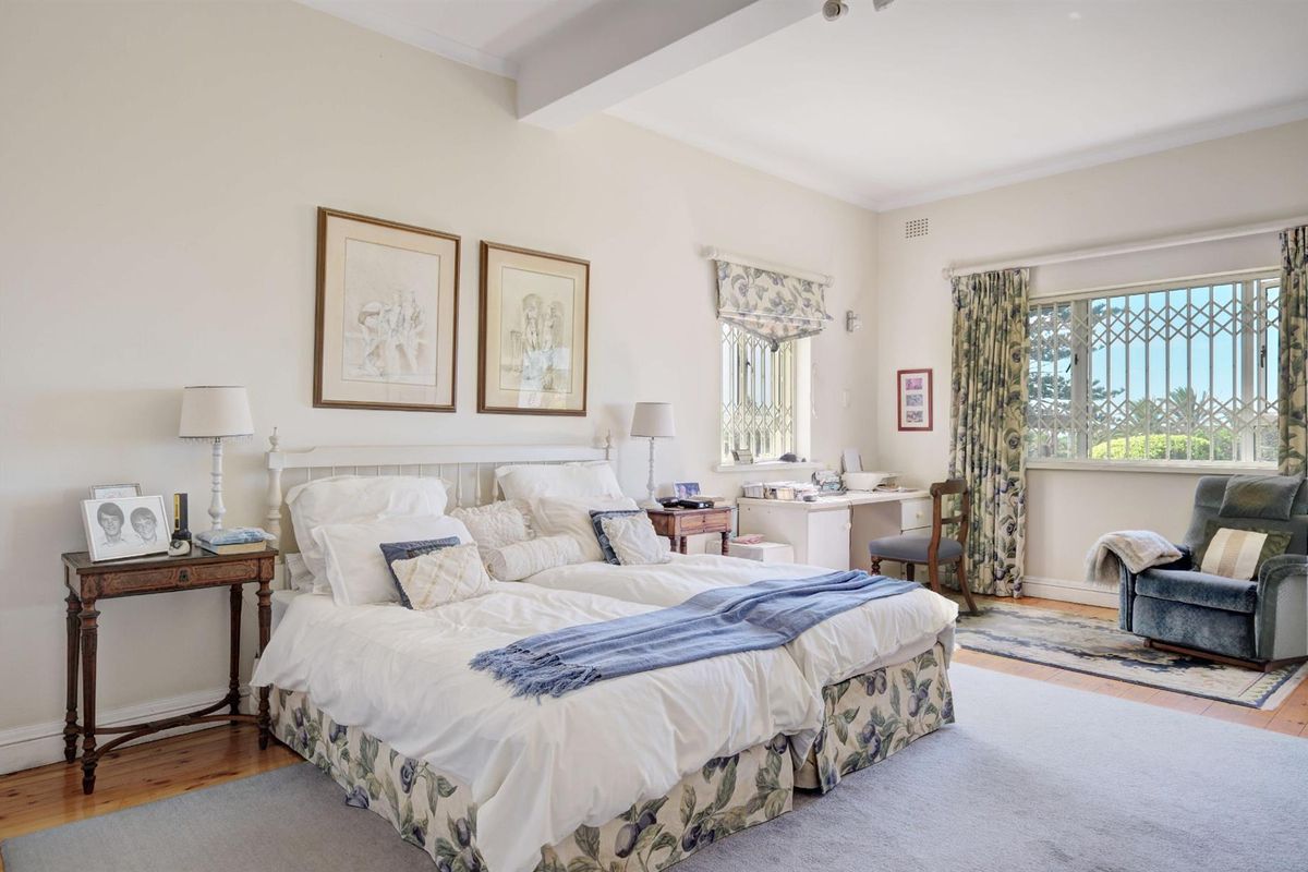 Spacious bedroom featuring polished timber flooring, large windows with security gates, and neutral wall finishes, offering a comfortable and well-lit living space.