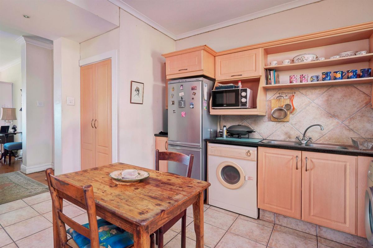 Compact kitchen featuring light wood cabinetry, tiled backsplash, integrated sink, and tiled flooring, with an adjacent built-in storage cupboard.