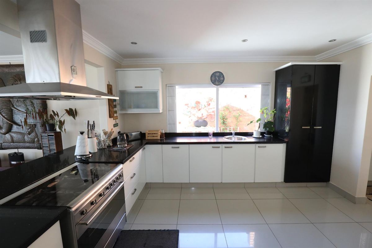 Modern kitchen featuring high-contrast black and white cabinetry, granite countertops, stainless steel extractor fan, and large format floor tiles.