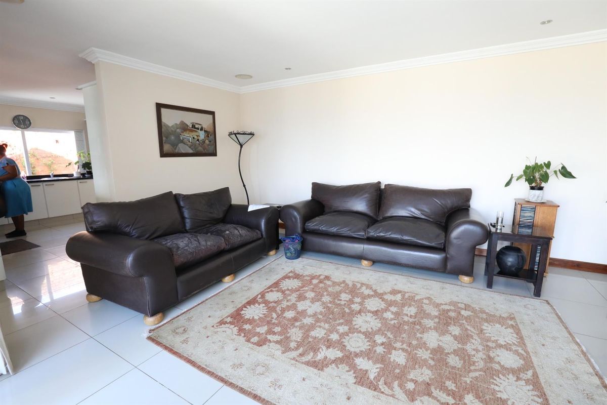 A spacious living area featuring tiled flooring and crown molding, with an open-plan layout connecting to the adjacent kitchen space.